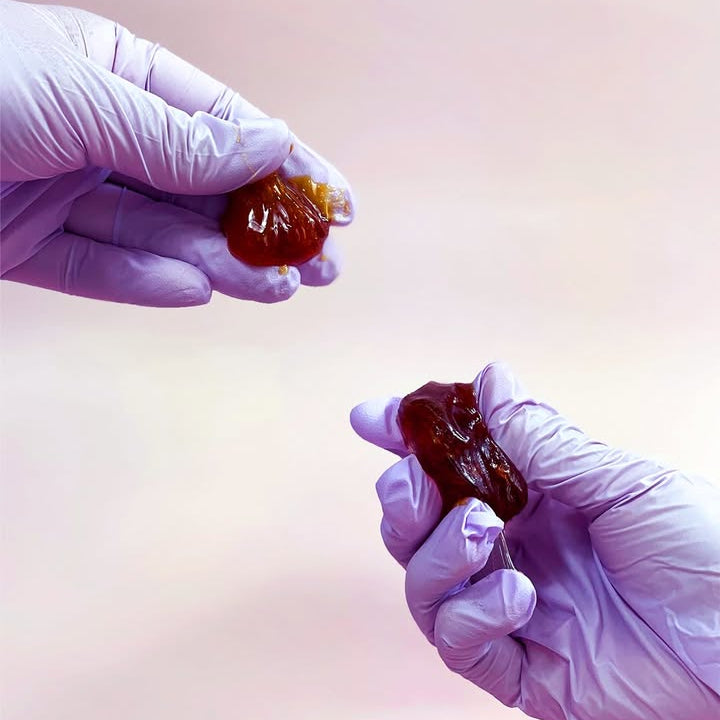 Two gloved hands holding paste against a light pink background