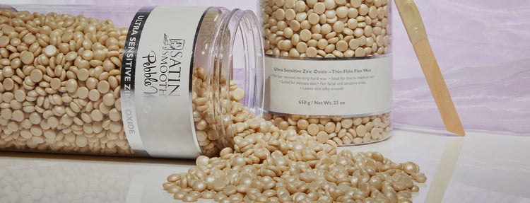 Satin Smooth Ultra Sensitive Zinc Oxide pebble wax beads spilled from jar for no-strip hair removal.