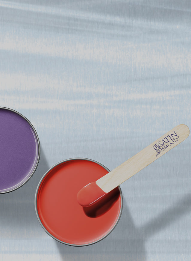 Satin Smooth red and purple hard wax tins with branded spatula on cool-toned background.
